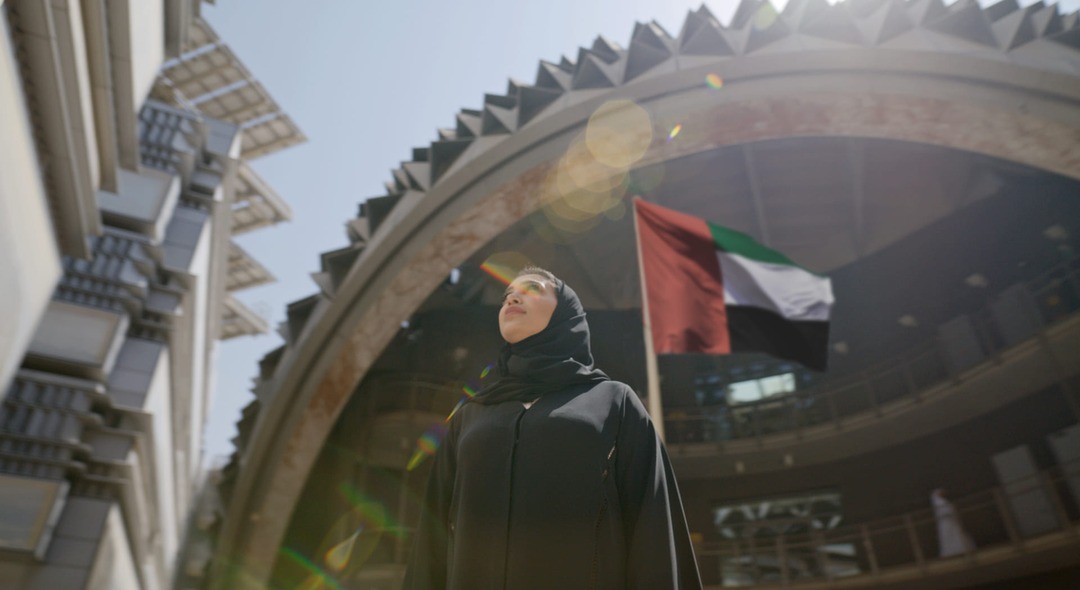 An Emirati woman looks up at the UAE flag at Masdar City, marking Emirati Women's Day.